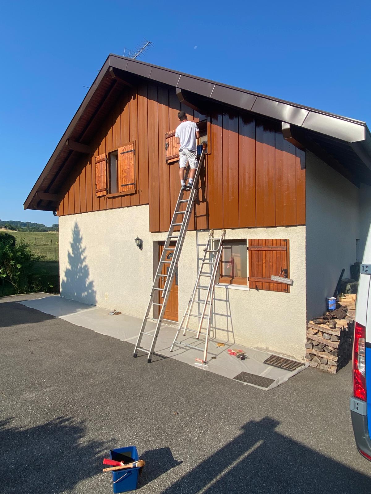 Peintre en train de rénover la façade en bois d'un chalet en Haute-Savoie