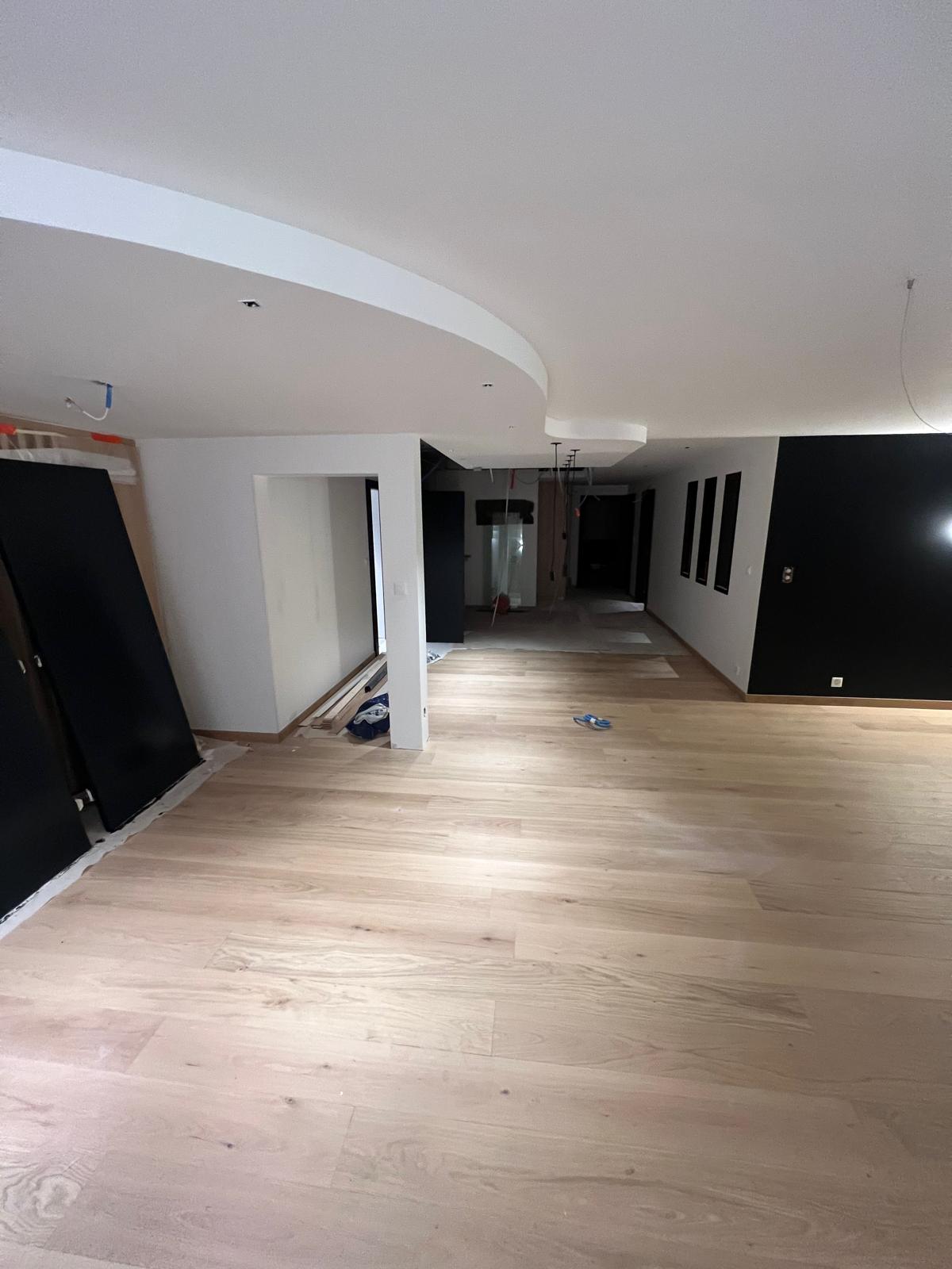 Grand plateau ouvert avec faux-plafond rond, mur noir et parquet chêne clair